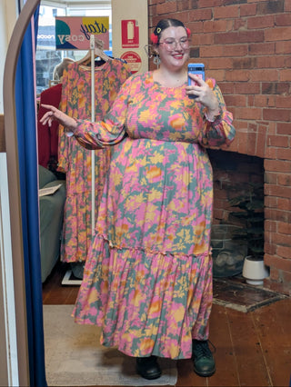 Person wearing a colorful floral dress taking a mirror selfie in a store.