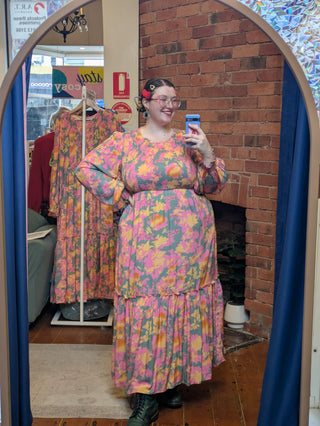 Person wearing a colorful floral dress taking a mirror selfie in a store.