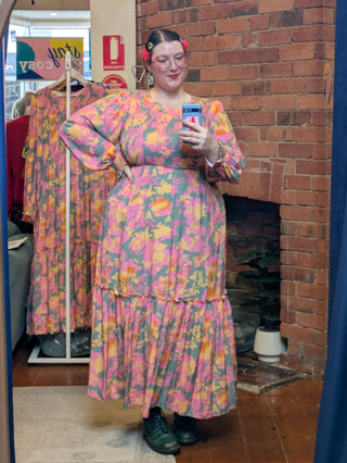 Person wearing a colorful floral dress taking a mirror selfie in a room with brick walls and wooden floors.