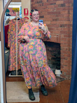 Person wearing a colorful floral dress taking a mirror selfie in a store.