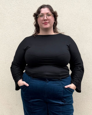 Person wearing a black top and blue velvet pants standing against a beige wall.