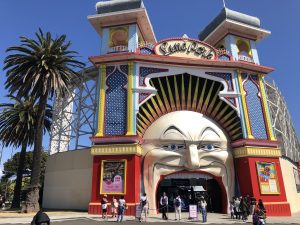 The giant face of St Kilda's Luna Park entrance against a backdrop of blue skies and palm trees.