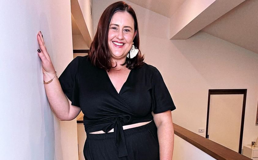 Stylist Amy smiles at the camera, looking put together and confident in a black wrap top and matching black pants, accessorised with a chunky earring.