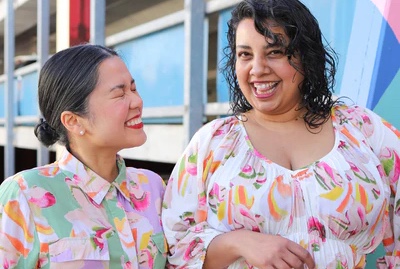 Two people smile joyfully wearing Khòlò's colourful clothing.